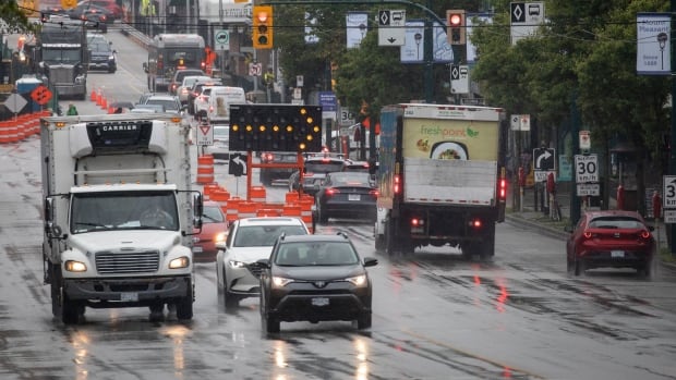 Cars drive down a rainy road, with construction visible behind them.