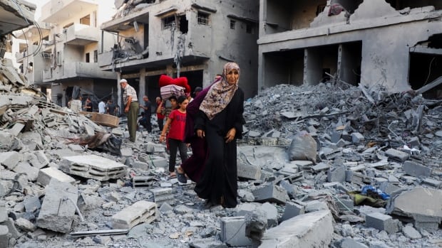 A woman with children walk through Gaza City's rubble.