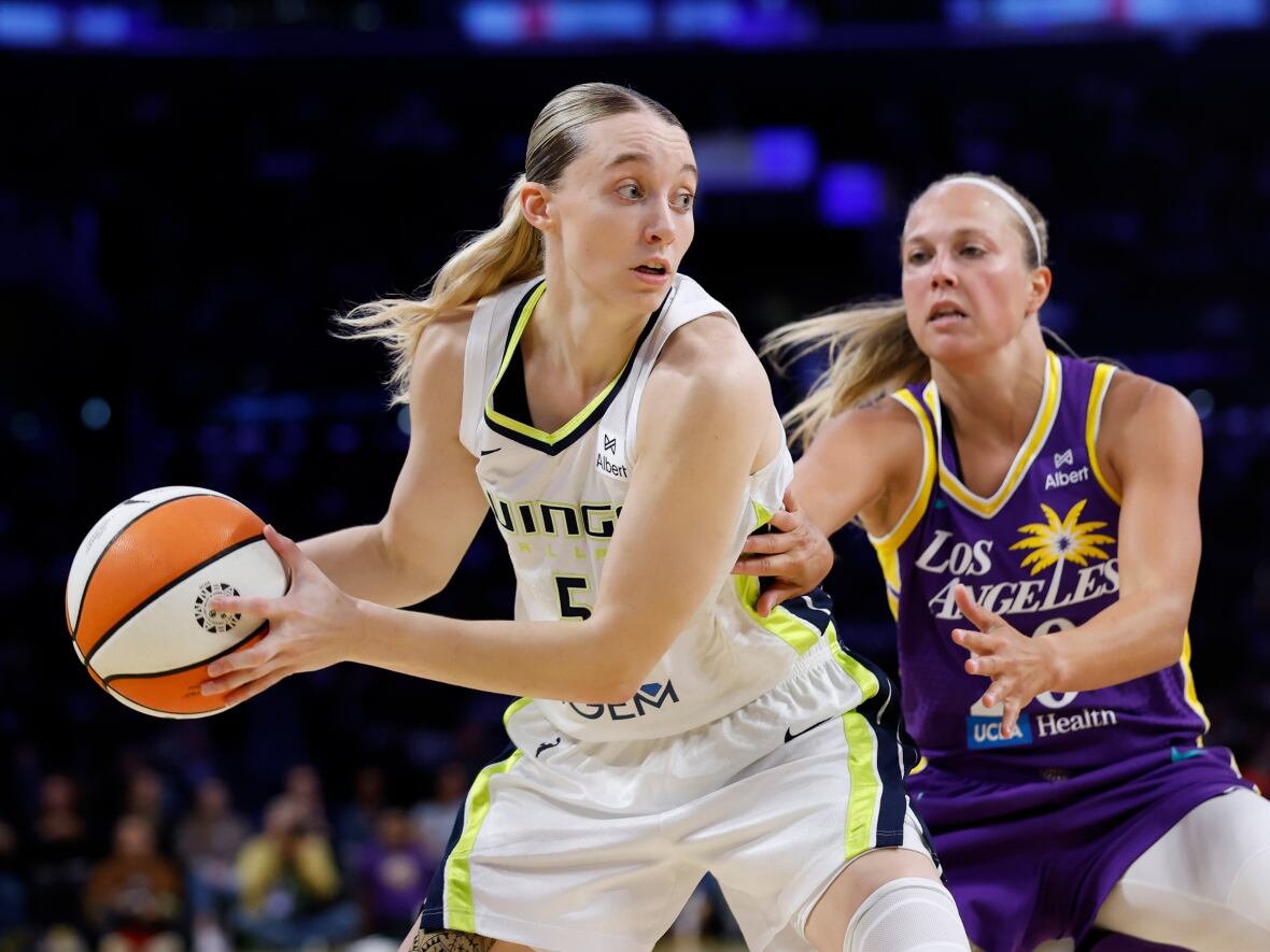 A woman in a white basketball uniform guards the ball from a woman in a purple uniform.