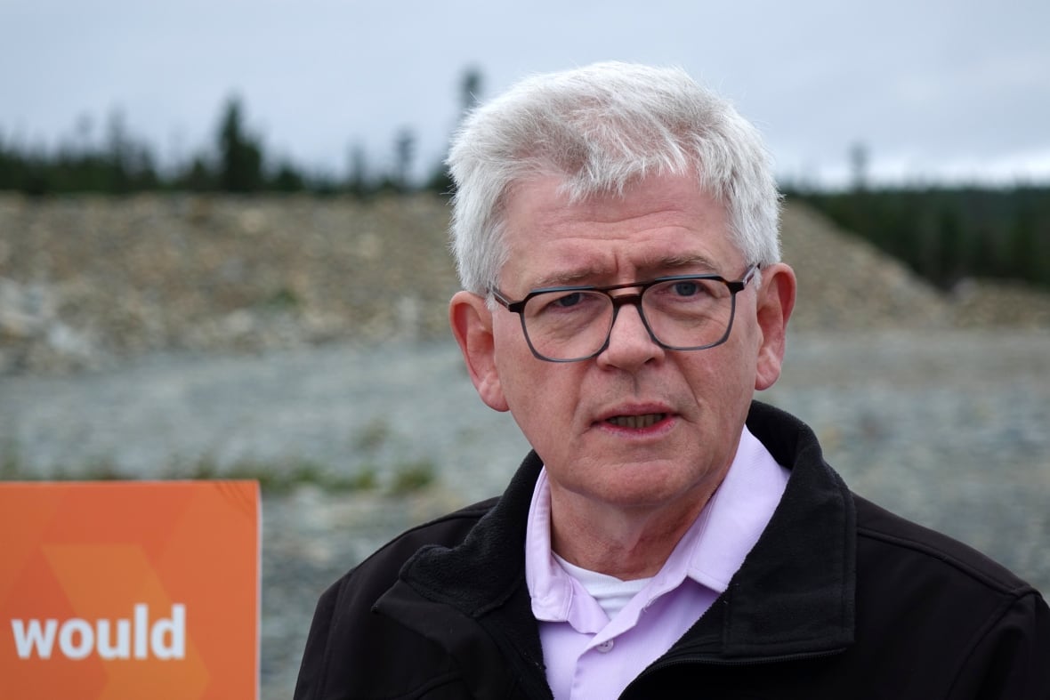 A man wearing a black sweater stands on a rocky patch of land.