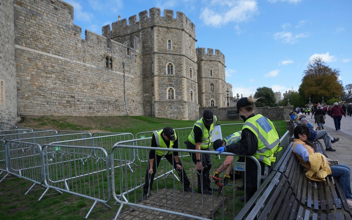 Men in yellow -reflective jackets work behind the metal fence bars. 