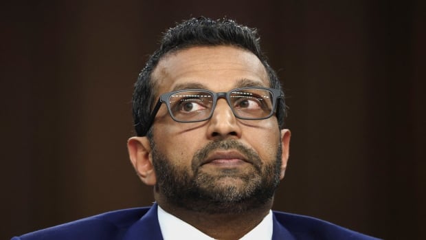 A man in a blue suit, red tie and glasses is pictured as he testifies before a panel.