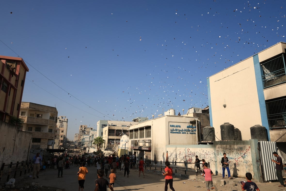 People run to collect leaflets being dropped from the sky.