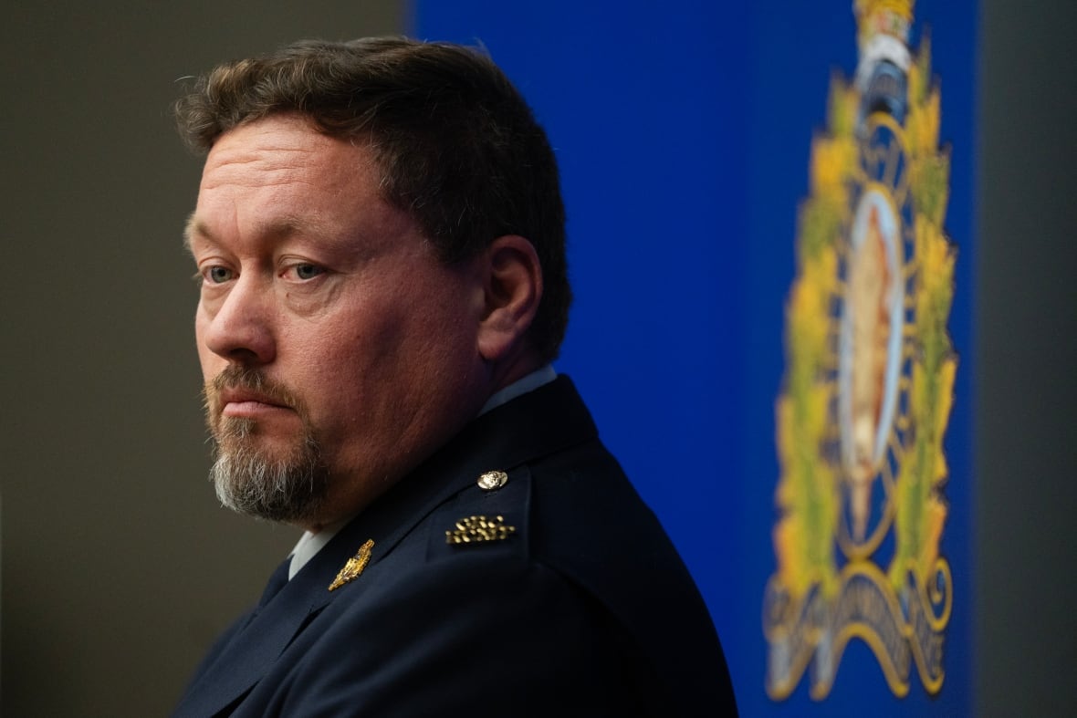A man in a police uniform looks over his shoulder with a sombre face.