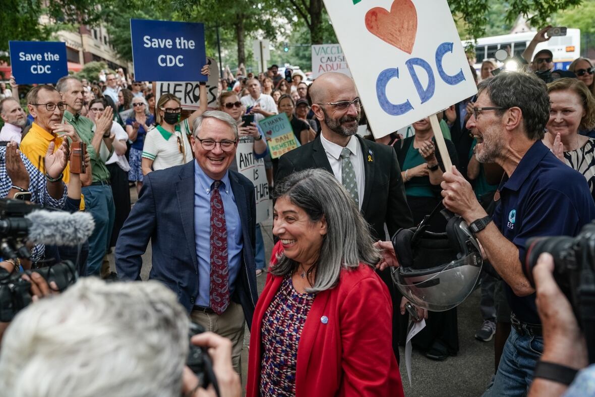 Several people are shown, men and women, in a foreign reference with signs behind them.