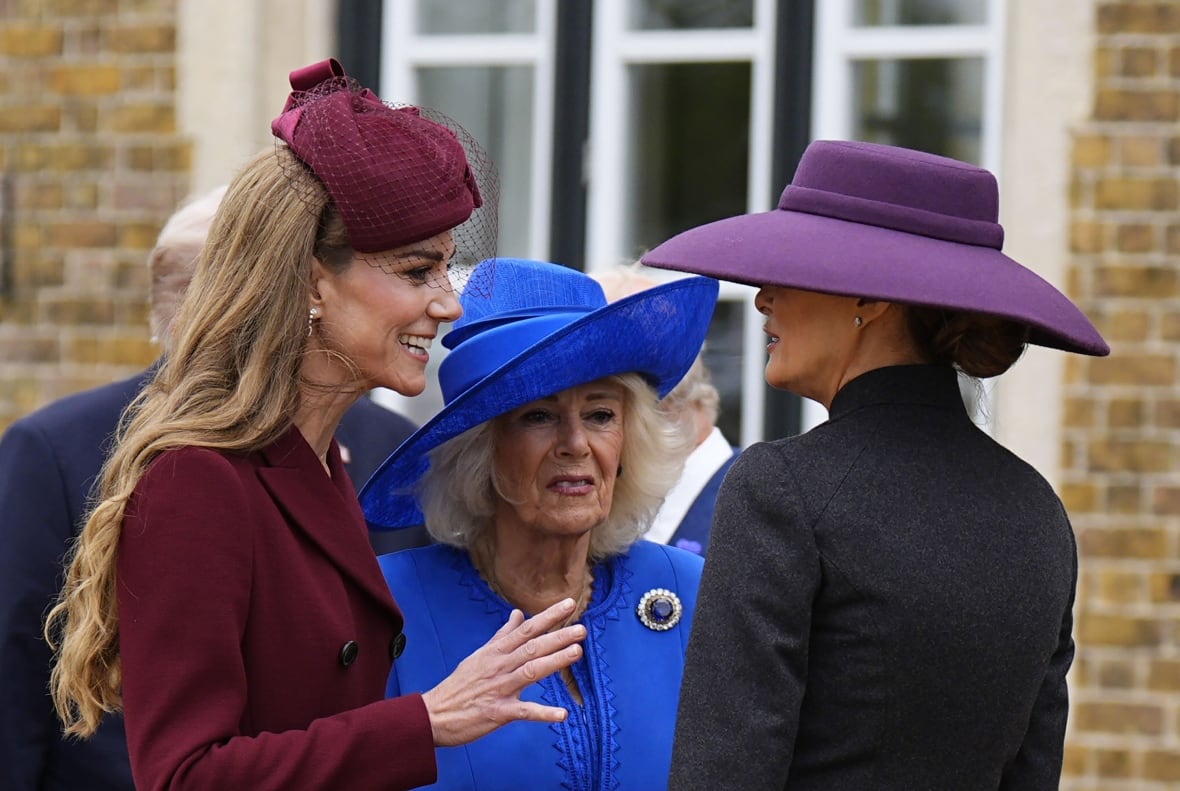Three women in formal dress and hats smile and talk together