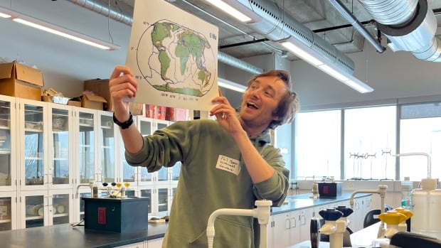 Man stands in front of a classroom holding up a map.