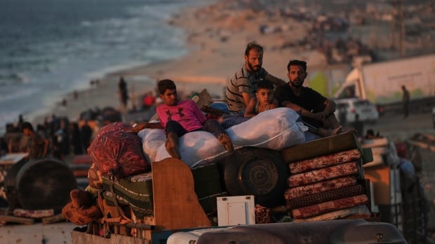Two adults and two chidlren ride on top of a truck packed with various belongings. 