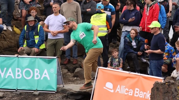 A crowd of people watch a person throw a stone into water outside.