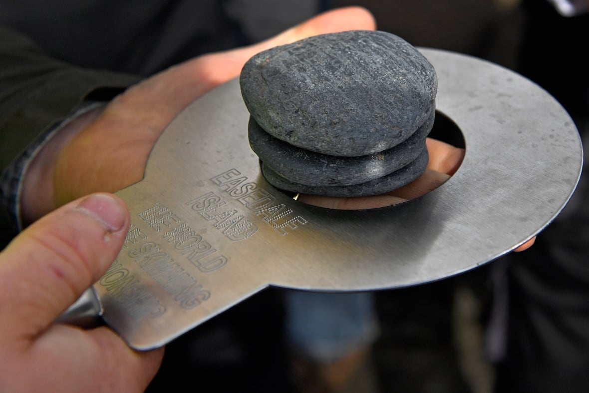 Small stones are seen closely, at the top of a round metal measurement tool.