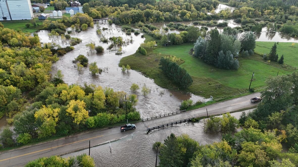 Un automóvil va sobre un puente rodeado de un arroyo desbordado.