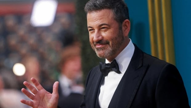 A man in a suit waves on a red carpet.