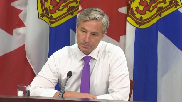 A man in a shirt and tie sits in front of a microphone.