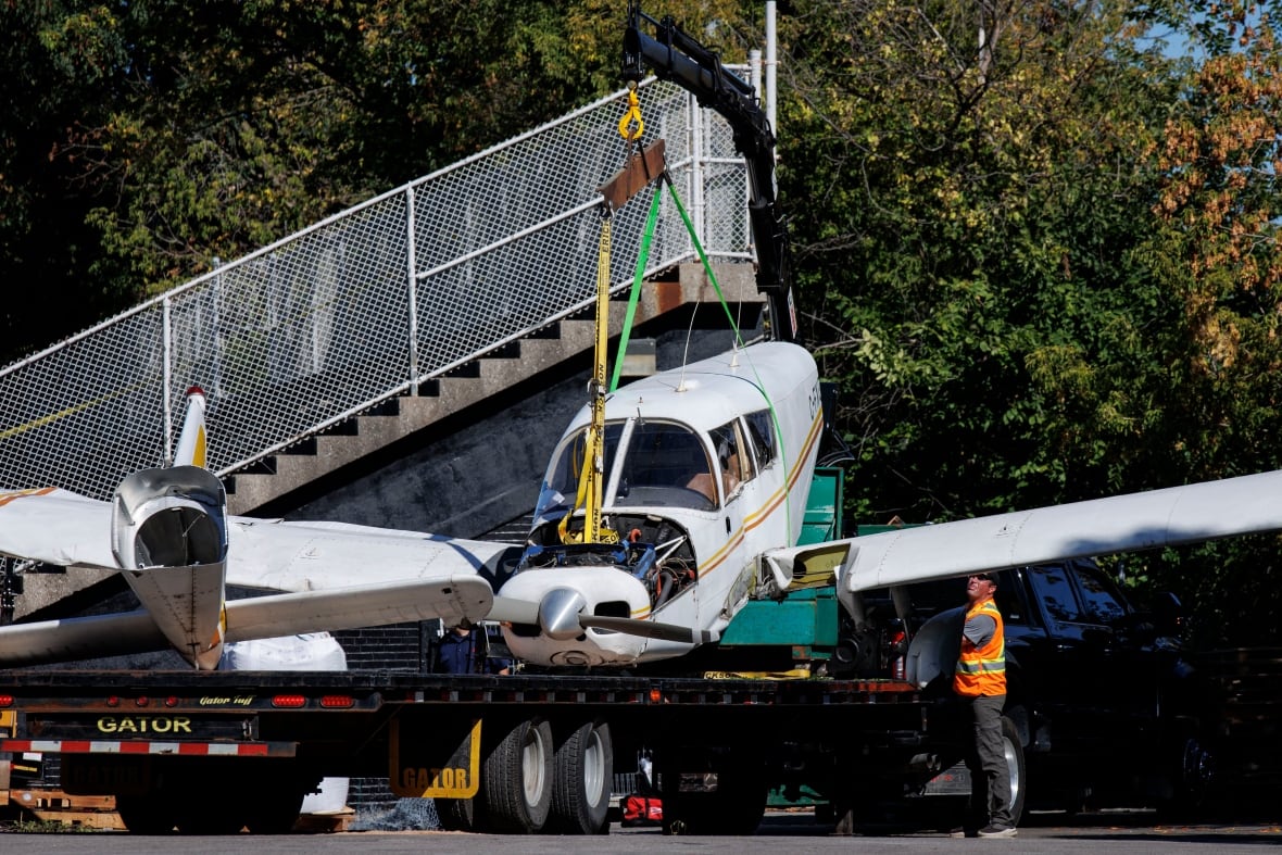 The higher person stands next to a small plane wreckage lined on the driver's bed, near the outside of the outside field bleacher.