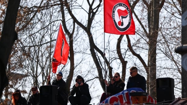 People gather among trees, waving red, white and black flags with anti-fascist symbols on them.