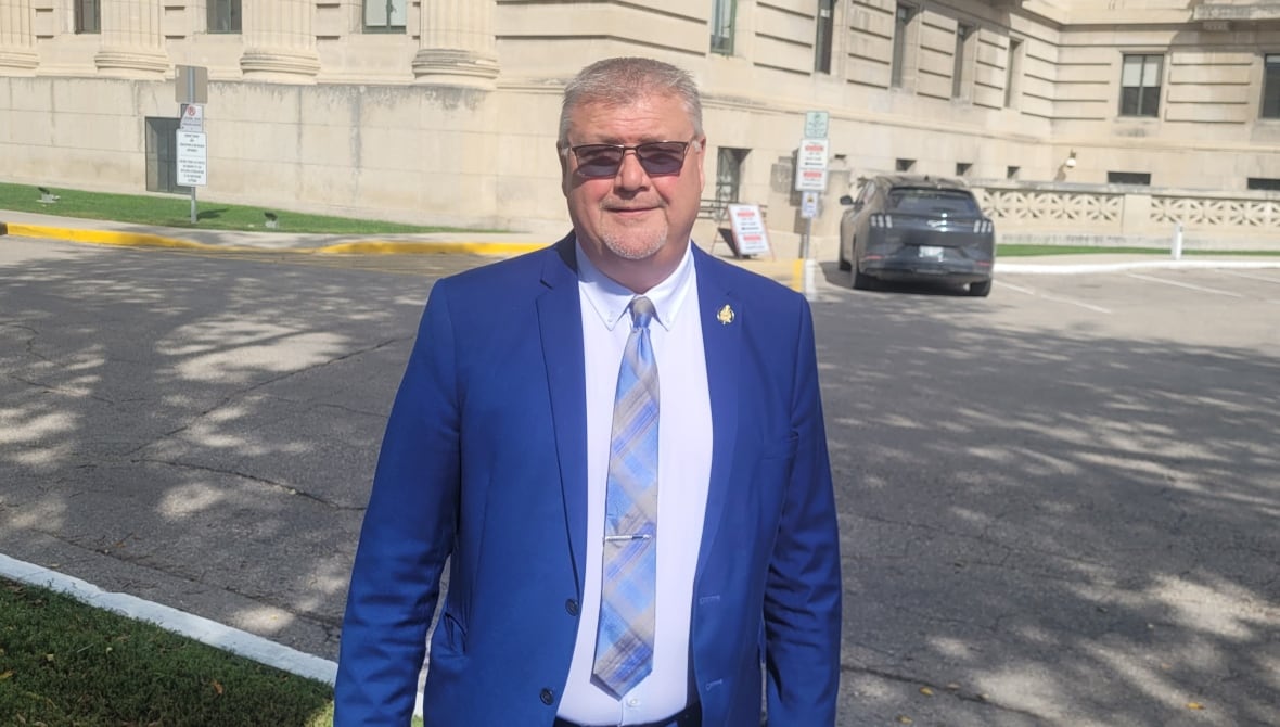 A man in sunglasses and a blue suit stands outside of the Manitoba Legislative building.