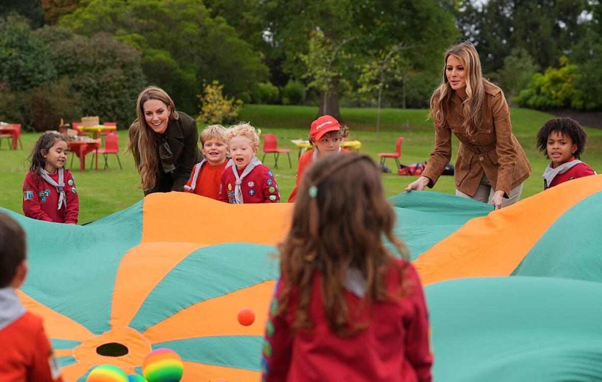 Two adults and seven children hold a colourful large cloth as they play a game on a lawn.
