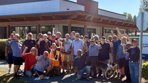 A group of employees stand outside a building and cheer.