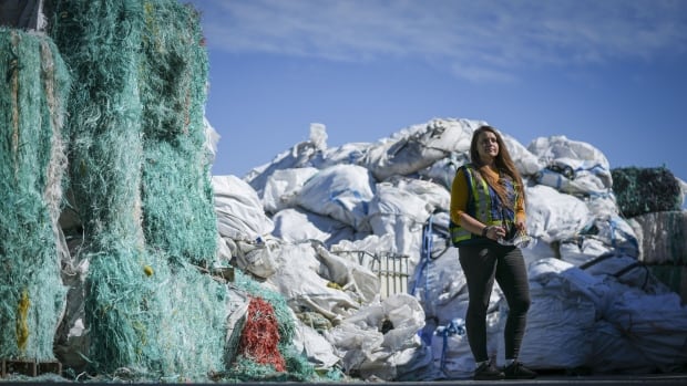 A woman wearing a neon construction vest stands in front of a mountain of yellow sacks full of fishing rope and other marine gear.