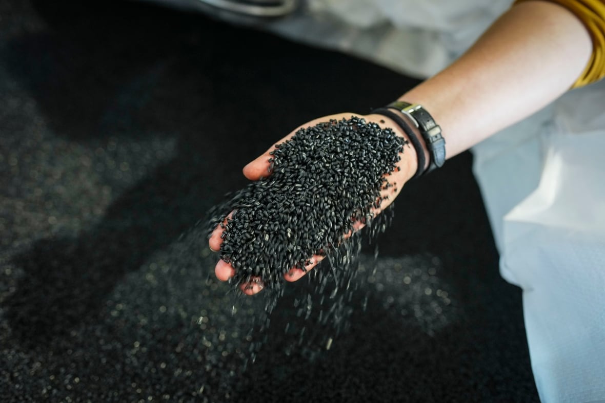 A hand holds tiny, black plastic pellets.