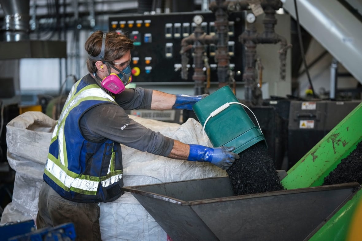 A warehouse worker places a bucket of pellets into a machine.