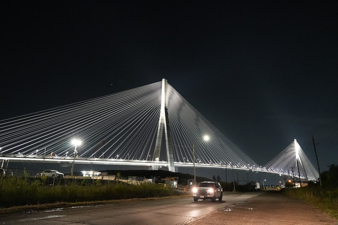 A cable stay bridge with its pillars, deck, rails and each cable illuminated in light.  Bright construction lights are also seen on the deck. 
