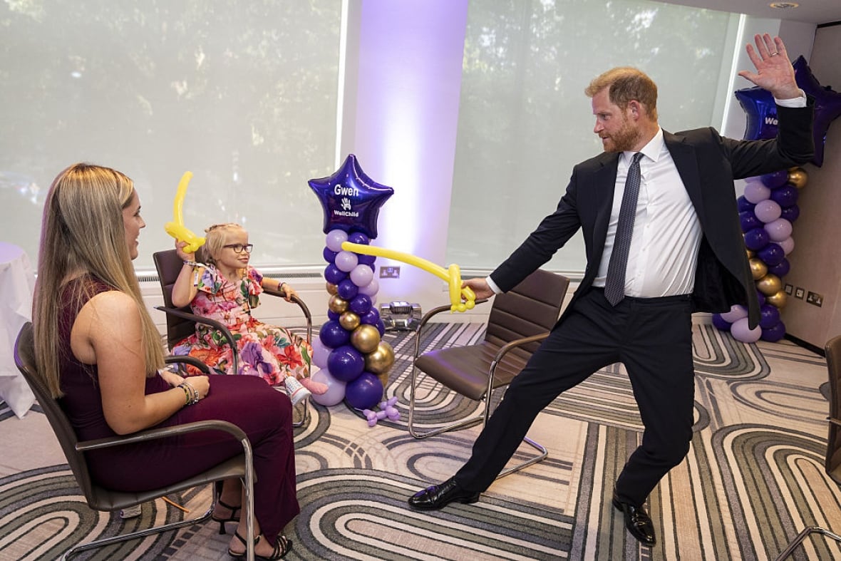 An adult does a play swordfight using a balloon with a seated child as another adult sits nearby.