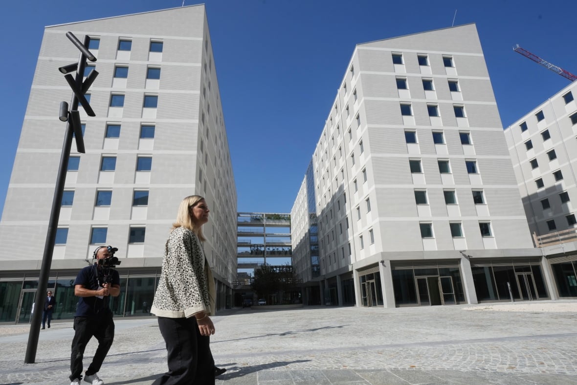 Two people walk through long white buildings.
