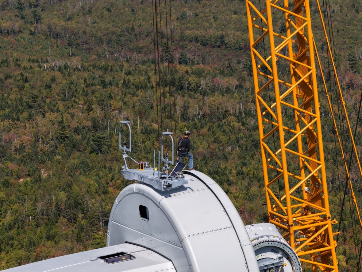 A worker stands at the top of a turbine hub to assist with the installation of blades at a wind farm.