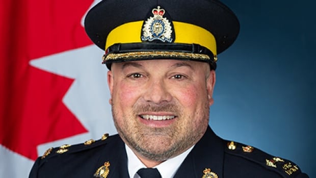 A man in a police uniform, wearing a hat smiles at the camera.