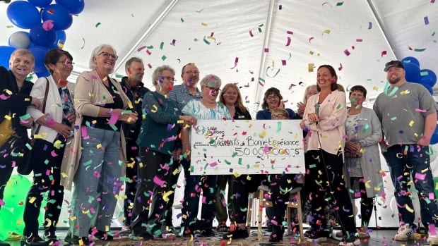 A group of people stand surrounding a large cheque