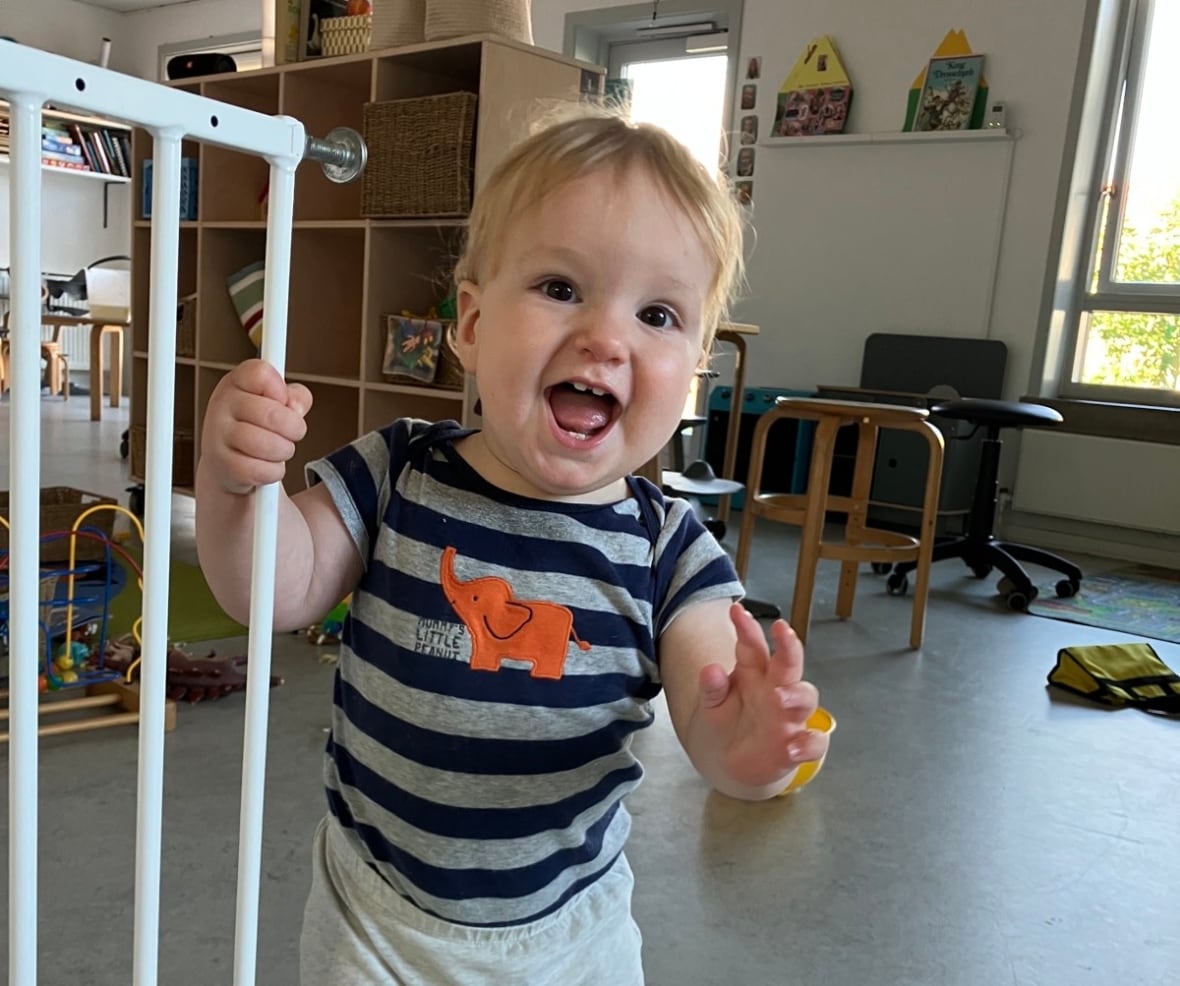 A small child smiles on the camera while holding the child's safety gate.