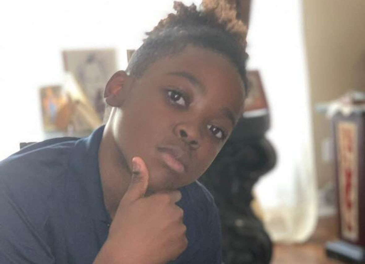 A young Black boy wearing a navy shirt holds his face as he looks seriously at the camera. 