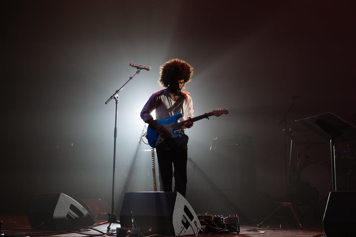 A black artist who plays guitar of the stage, enlightened by the point of view.