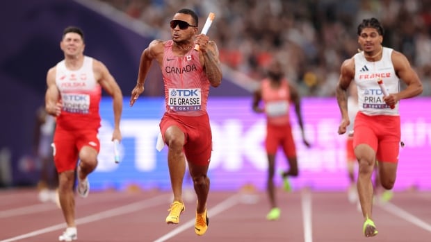 A male sprinter runs with a baton during a relay race inside a stadium.