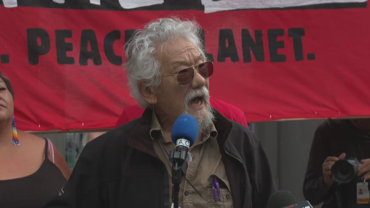 David Suzuki, a man in his 80s with grey beard and hair, speaks passionately into a microphone on a stage outside in downtown Toronto in September