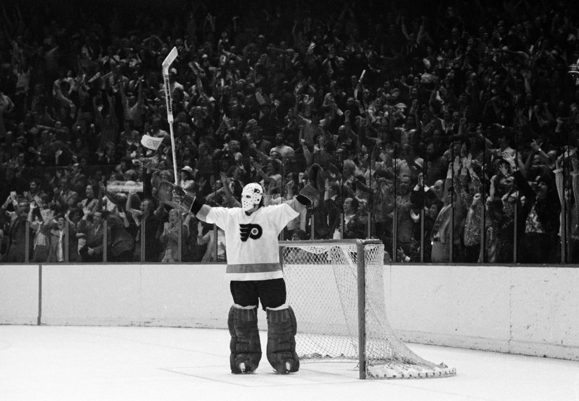 A male ice hockey goalie holds up his arms in celebration as fans cheer from their seats.