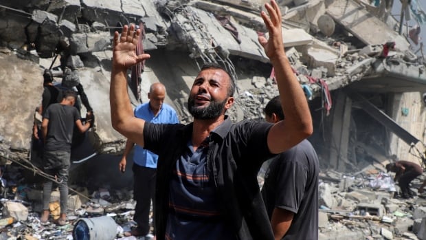 A man puts his hands up as people around him react to the damage to a building from an airstrike.