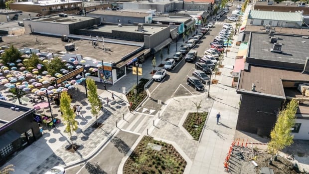 A birds eye view photo which shows a new Fraser Highway One-Way, pedestrians walking in downtown, shops, and a colourful canopy of hanging umbrellas. 