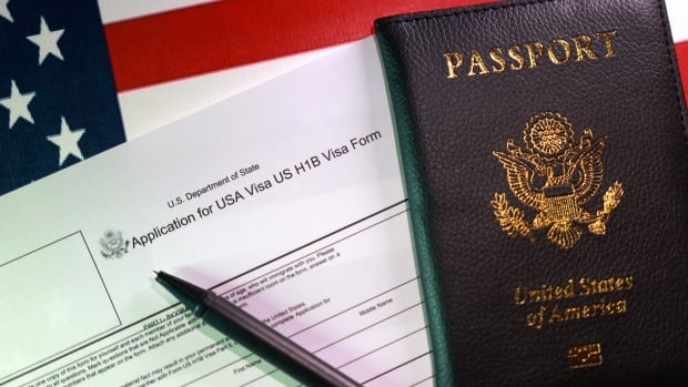 A pen, passport, and visa form are laid on top of a U.S. flag.