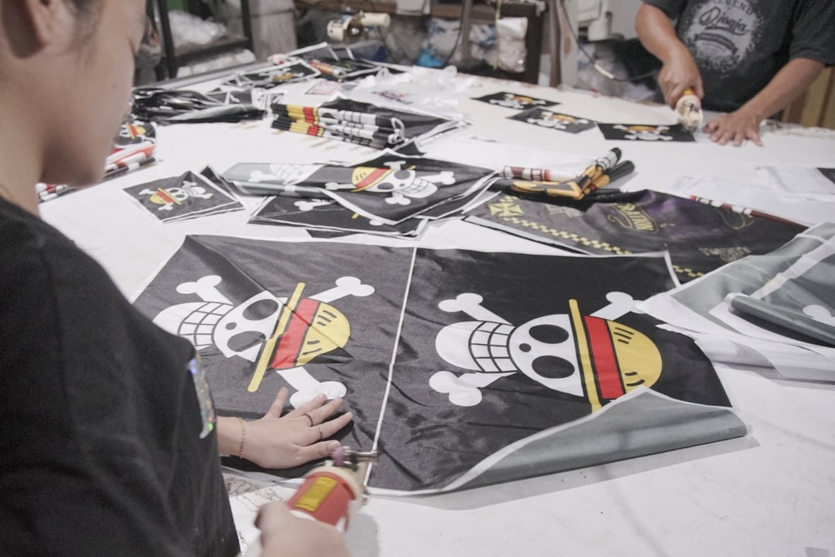 An individual is seen cutting out black flags that have a skull wearing a starw hat on it