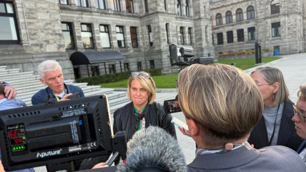 Elenore Sturko speaks with reporters outside the B.C. Legislature in Victoria as cameras and microphones surround her during a media scrum.