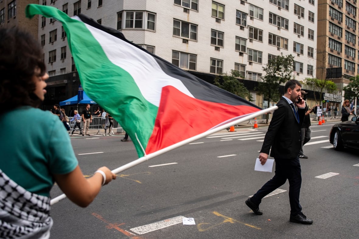 A woman with dark hair waving a flag on a crowded city street as a man wearing a suit that holds a mobile phone on his ear.
