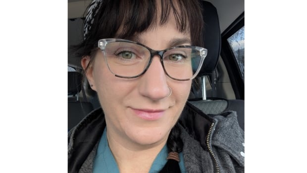 A woman wearing glasses smiles for a selfie, taken in a car