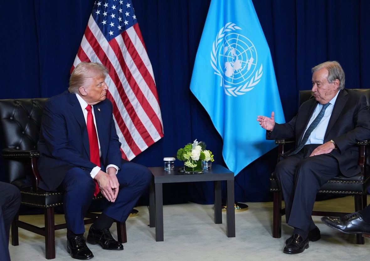Donald Trump, the left, and the Secretary -General of the United Nations Antonio Guterres, sit on chairs with the flags of the United States and the United Nations in the background between them. 