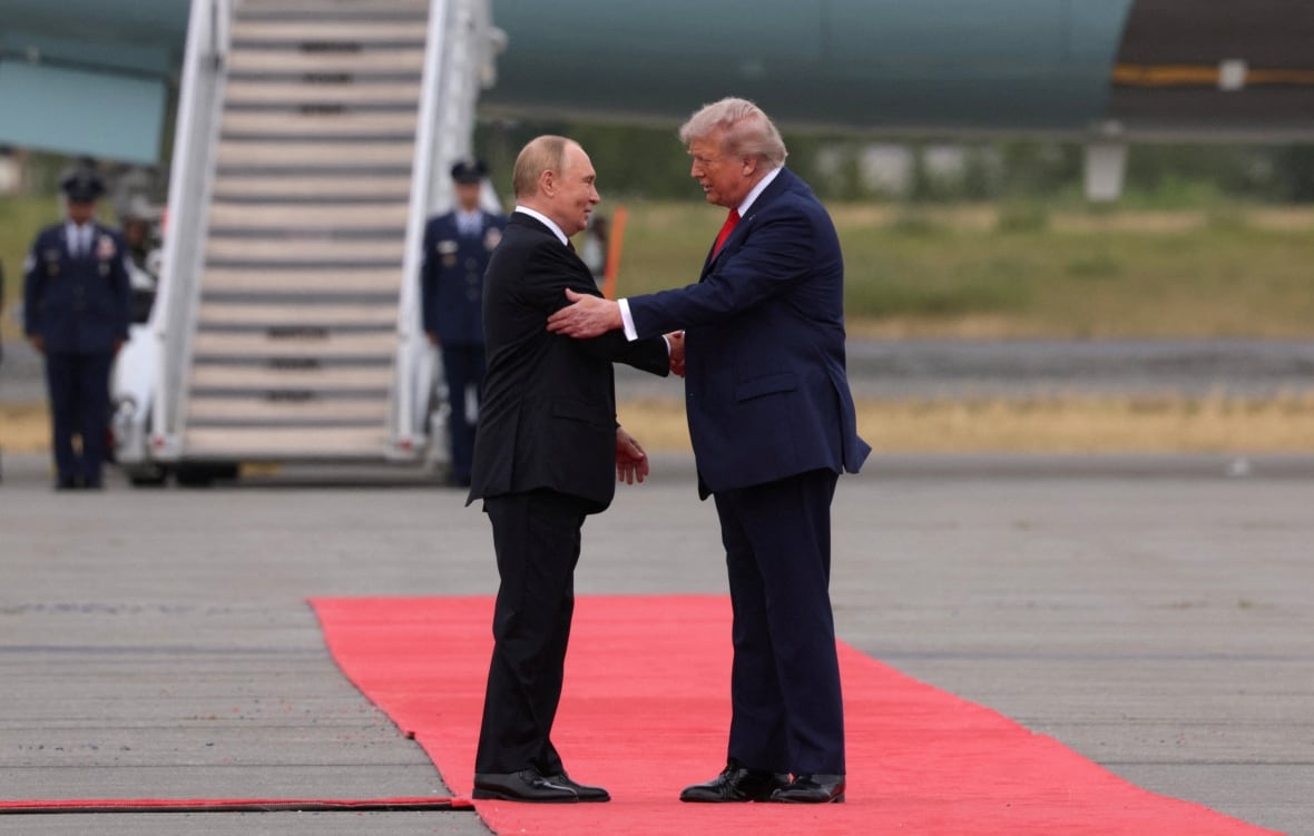 Two men meet and shake back a red rug at the airport runway, with a plane behind them