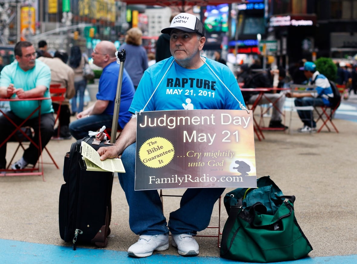 A man sitting in a crowded city plasma, wearing a banner reading 