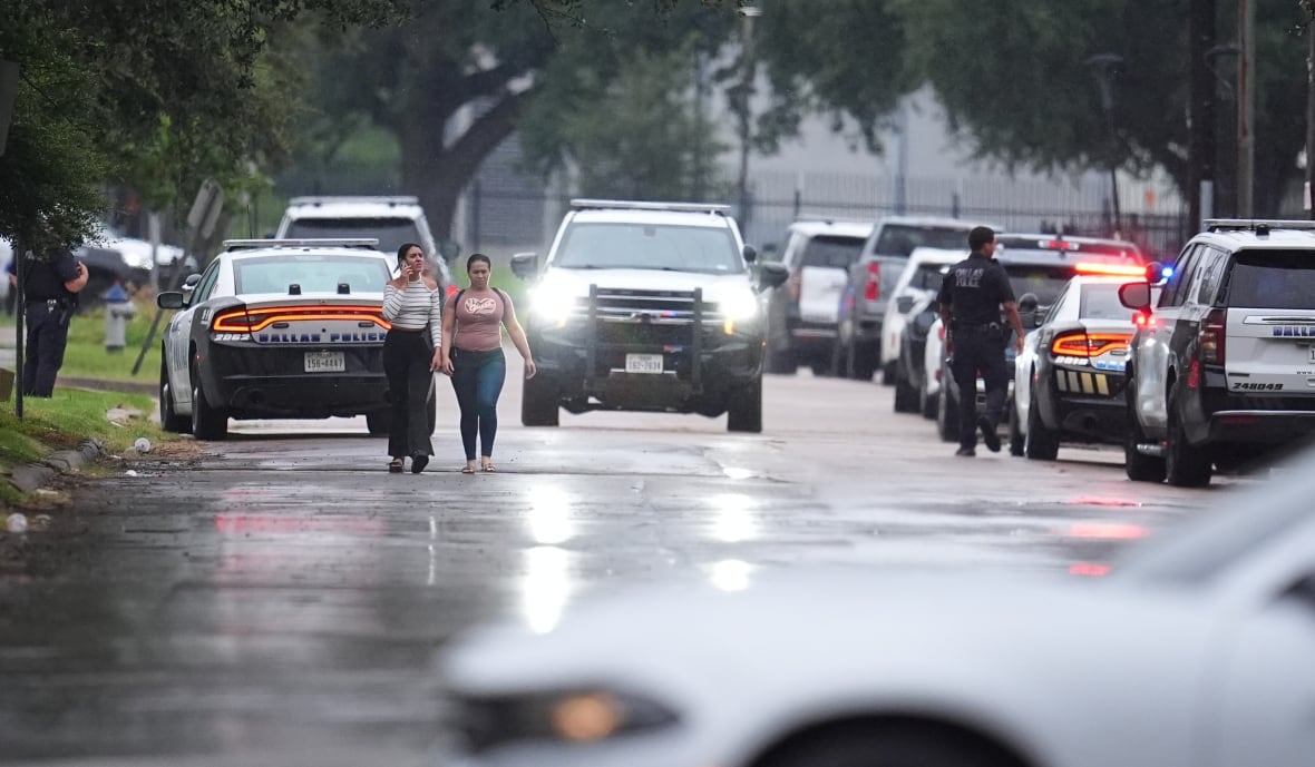 People walk along a road bordered by cars.