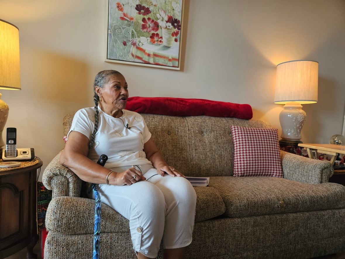 An older woman with a cane sits on a couch