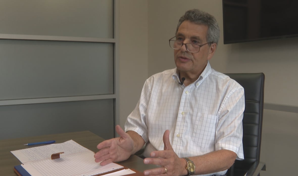 A middle aged man with glasses speaks while seated at a board room table